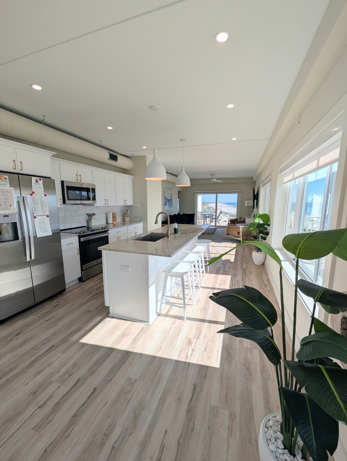 Bright vacation rental kitchen with a white island, bar stools and ocean views beyond the living area