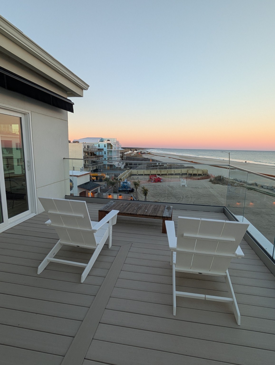 White balcony chairs overlooking the ocean under a soft pink sunset sky